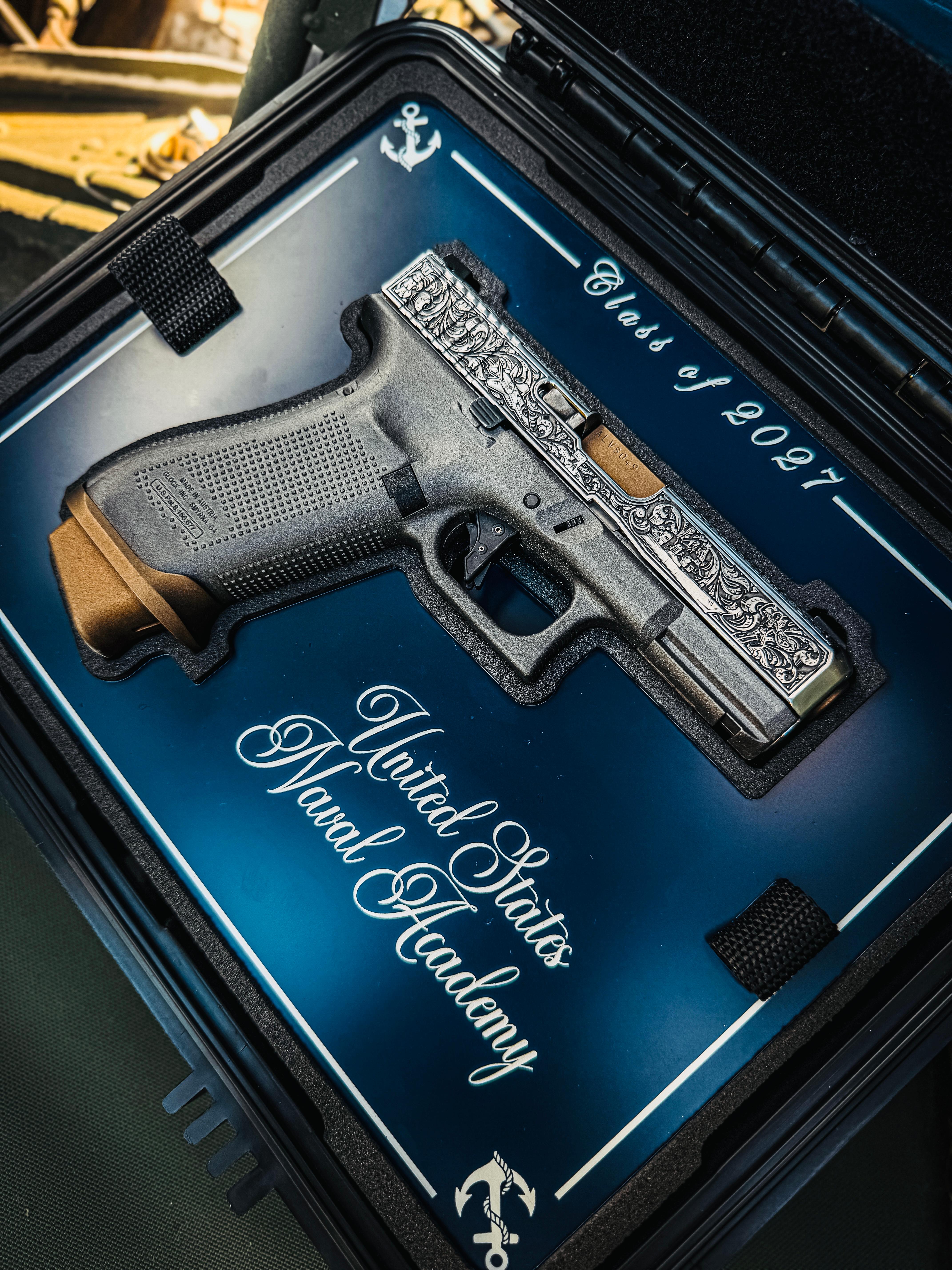 USNA Class of 2027 GLOCK 19X V — leaning against weathered blue and yellow surface