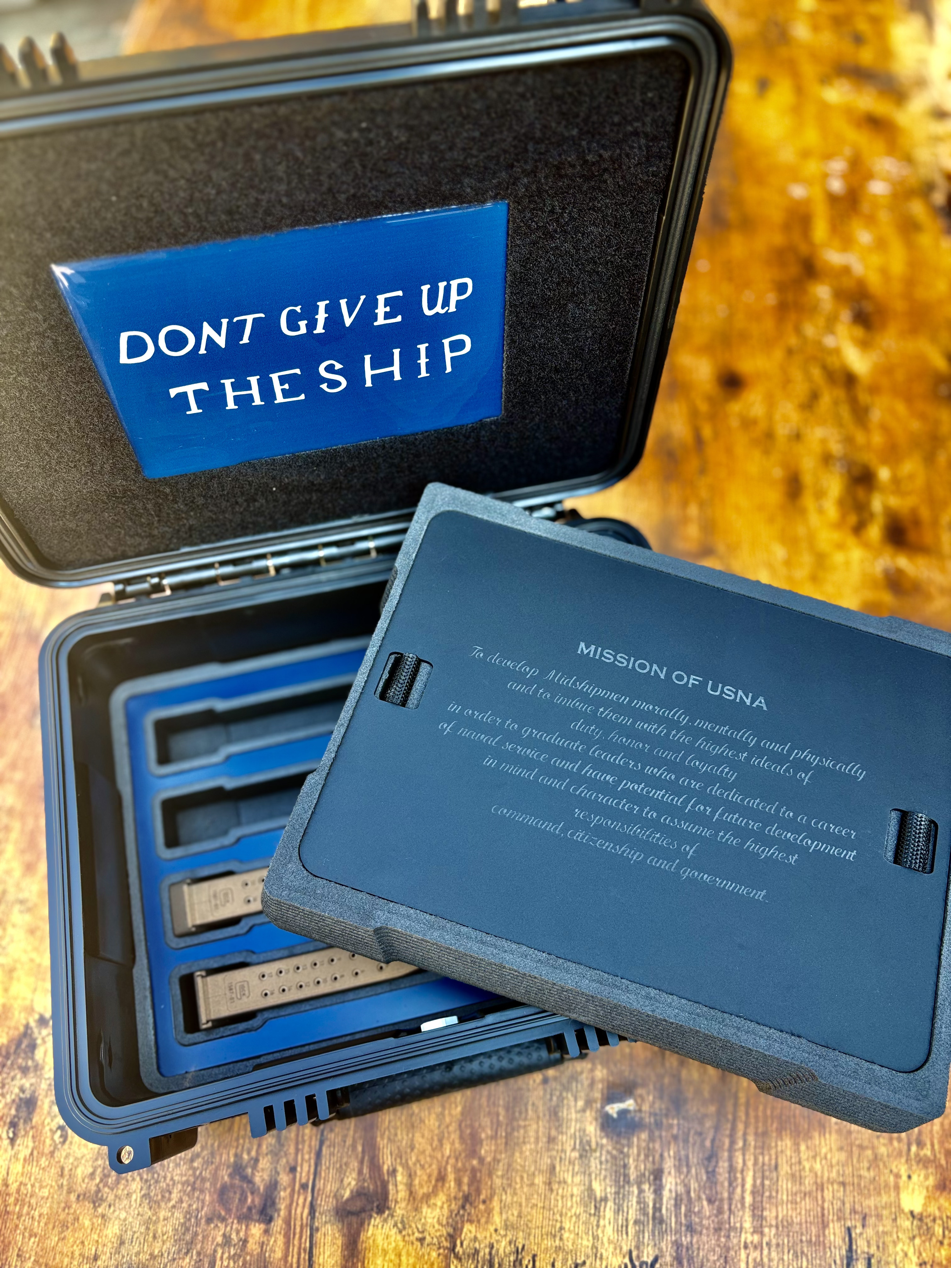USNA Class of 2027 presentation case — “Don't Give Up the Ship” lid panel with the engraved “Mission of USNA” foam insert lifted above the magazines