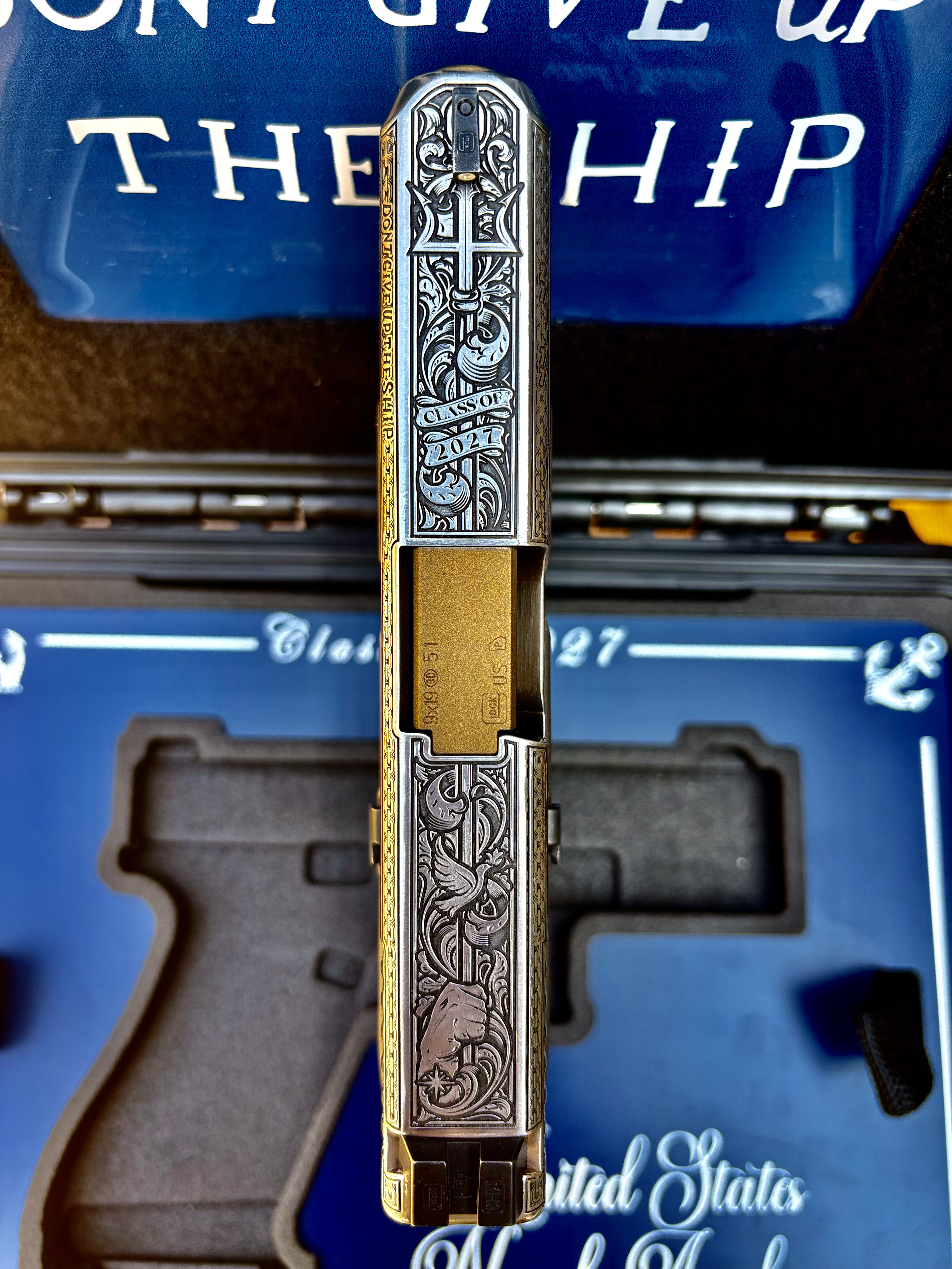 USNA Class of 2027 GLOCK 19X V — top-down view of the engraved slide showing the trident, “Class of 2027” banner, and “Don't Give Up the Ship” side inscription above the open presentation case